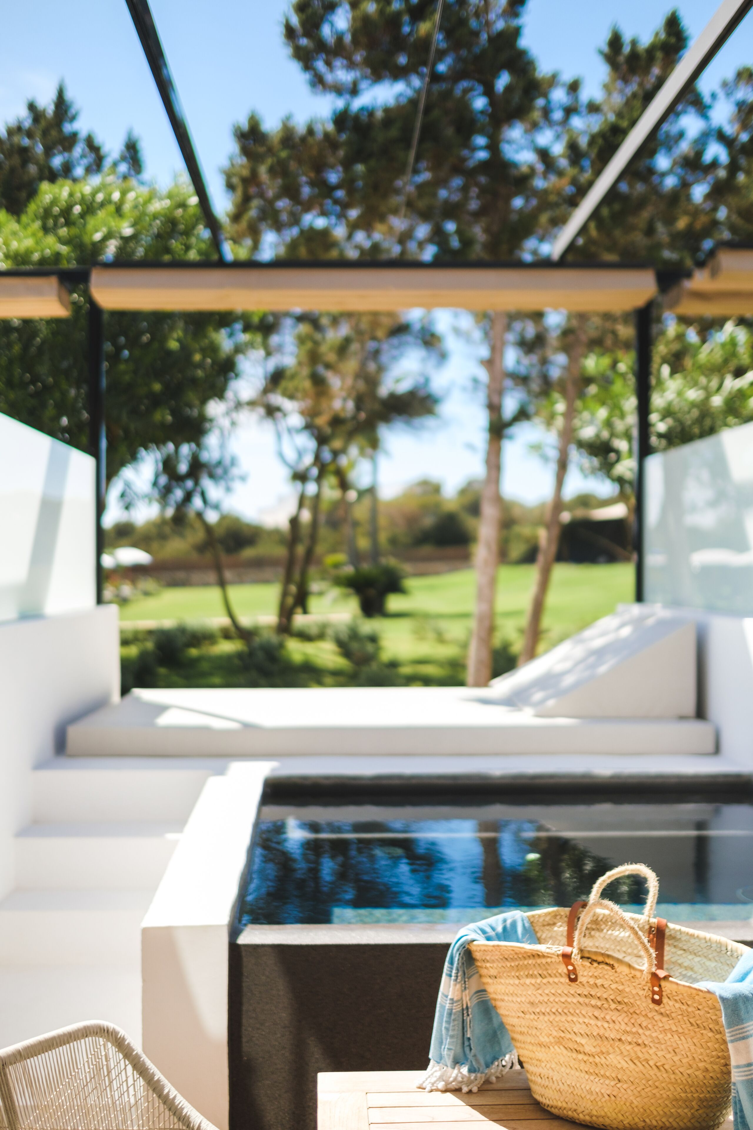 A modern outdoor seating area with a pool, a wicker basket, and a view of a green landscape.