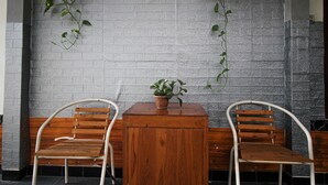 A seating area with two wooden chairs and a table, a potted plant on the table, and a textured wall behind. - Capital O 2258 Santana Syariah Guest House (Surakarta)