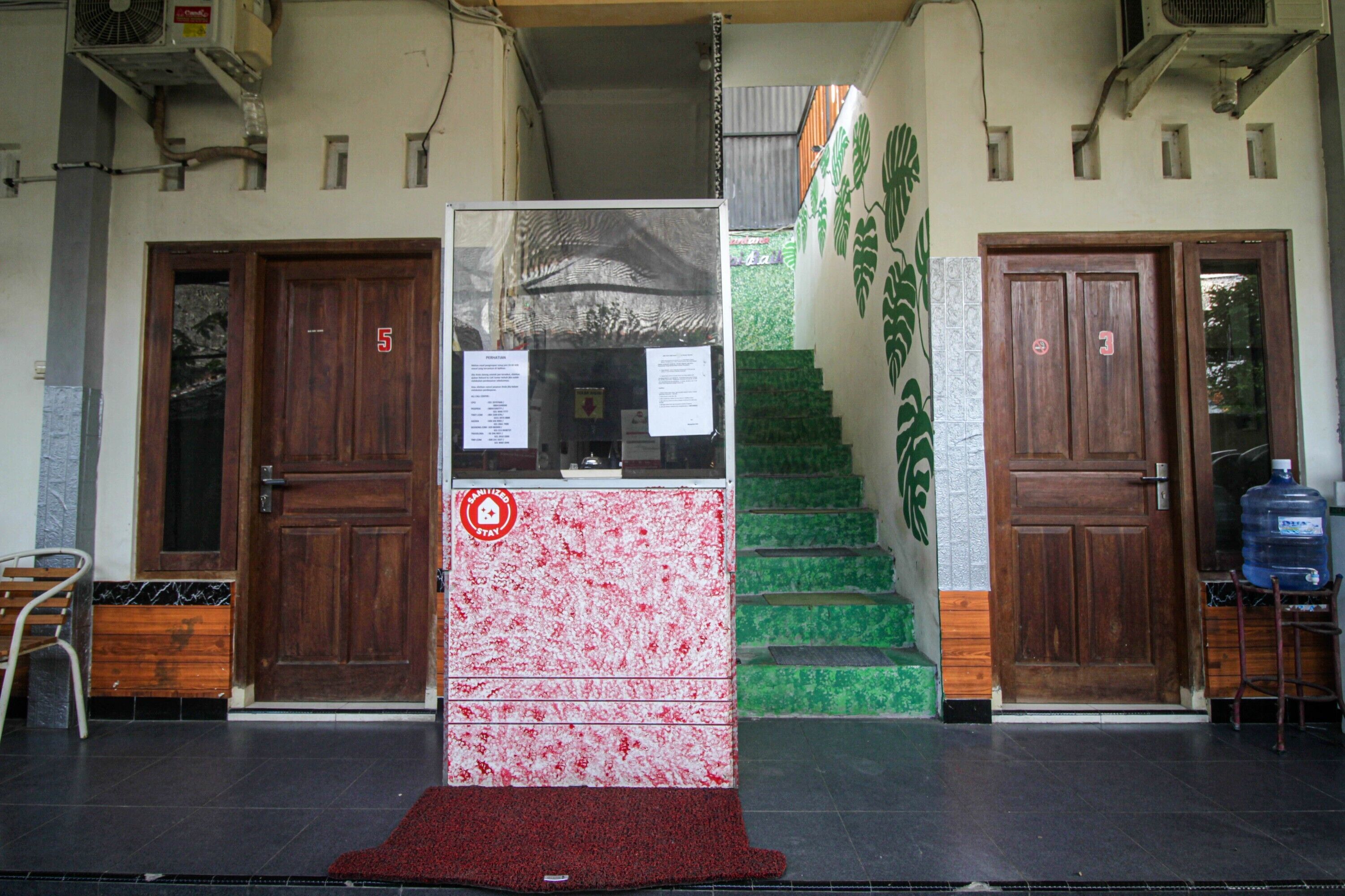 A building entrance with two wooden doors, a red mat, and a staircase with green steps.