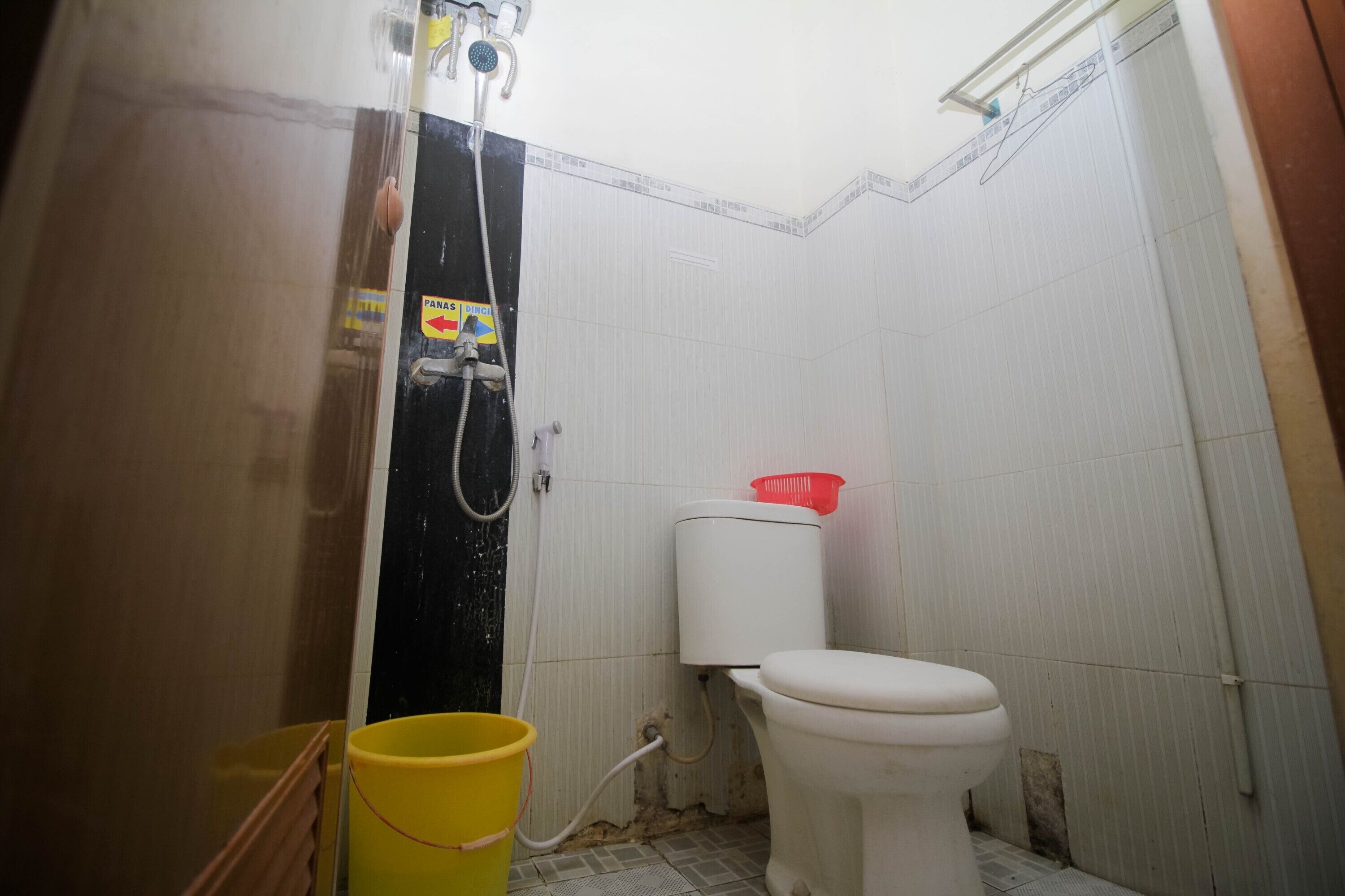 A small, narrow bathroom with a toilet, a shower, and a yellow bucket.