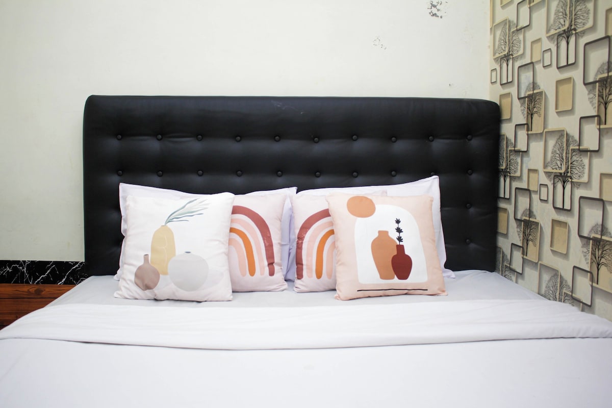 A bed with a black upholstered headboard, white bedding, and three decorative pillows with abstract designs.