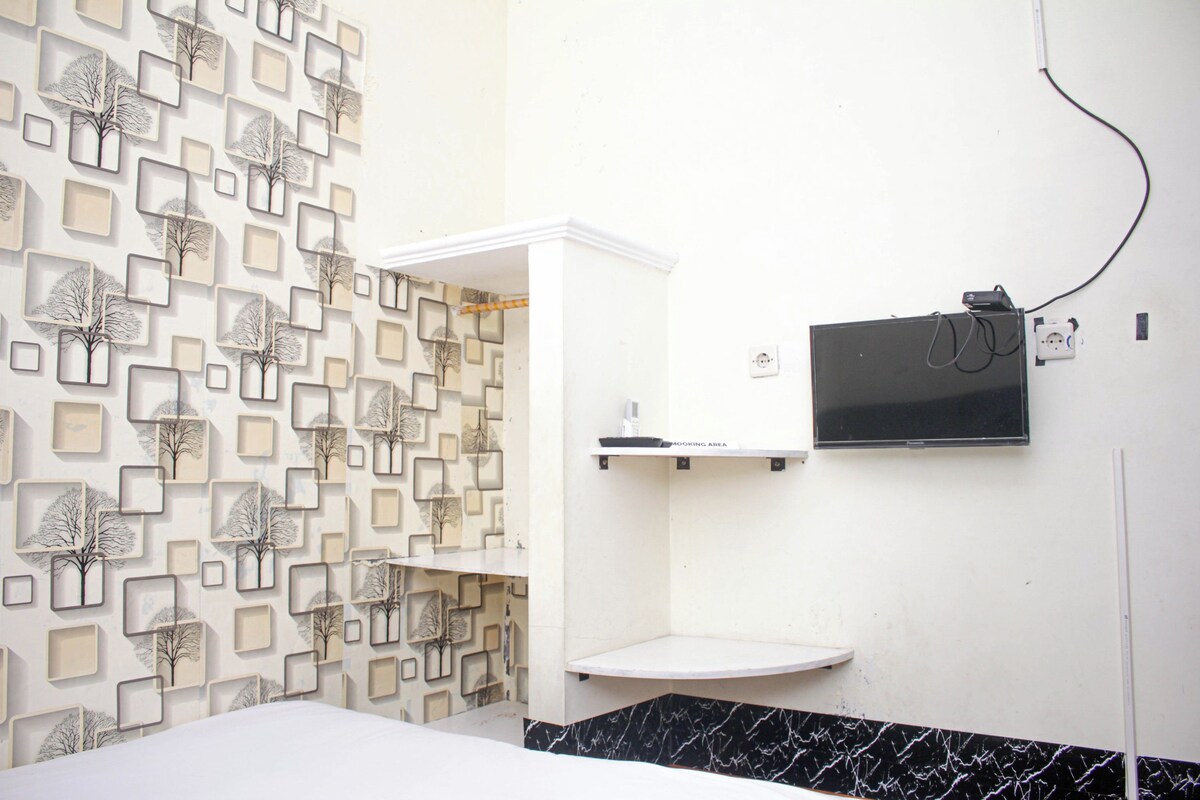 Baño de hotel con pared estampada, lavabo blanco y televisor de pantalla plana montado en la pared.