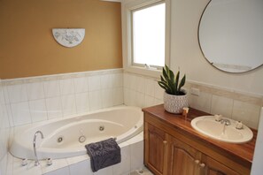 Een badkamer met een bad, wastafel, spiegel en raam.