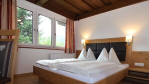A wooden-framed bed with white bedding, two bedside lamps, and a view of greenery through a window.