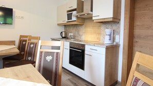 A compact kitchen with a microwave, stove, and coffee maker. There is a dining table with chairs and a TV mounted on the wall.