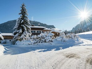 Schneebedeckte Landschaft mit einem Holzhäuschen, einem schneebedeckten Baum und blauem Himmel.