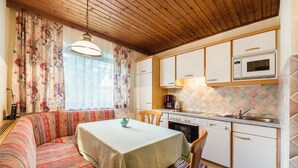 A cozy kitchen with a dining area, wooden ceiling, and a colorful patterned sofa.
