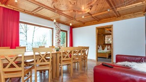 A wooden dining area with a table and chairs, a red sofa, and a view of trees through the window. - Great Group Holiday Home (Neukirchen am Grossvenediger)