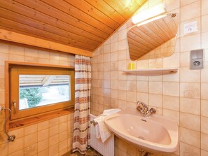 A bathroom with wooden ceiling, a window with a view, a sink, and a mirror. - Cozy Apartment in Wald- Konigsleiten (Wald im Pinzgau)