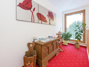 A room with a wooden cabinet, a red carpet, a window with a view of trees, and a painting of red flowers on the wall. - Cozy Apartment in Wald- Konigsleiten (Wald im Pinzgau)