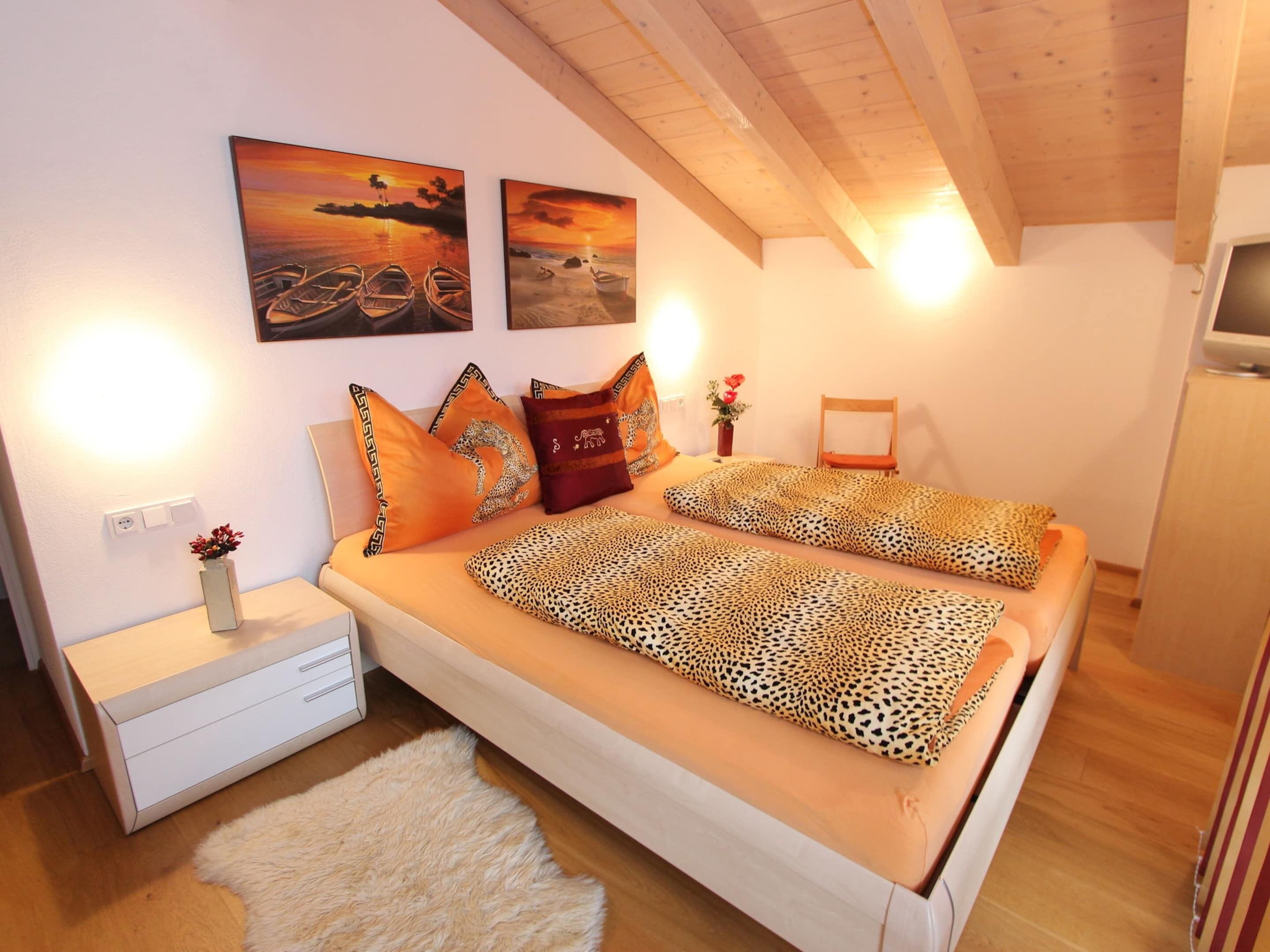 Um quarto com cama, mesas de cabeceira, televisão e obras de arte na parede.