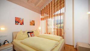 Ein Schlafzimmer mit Bett, Kissen, Nachttisch und Lampe. An der Wand hängen zwei Gemälde und ein Fenster mit Jalousien.