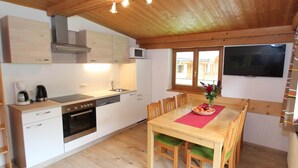 A compact kitchen with white cabinets, a microwave, and a stove. There is a dining table with chairs and a TV mounted on the wall. - Apartment in Viehhofen Near Ski Lifts (Viehhofen)