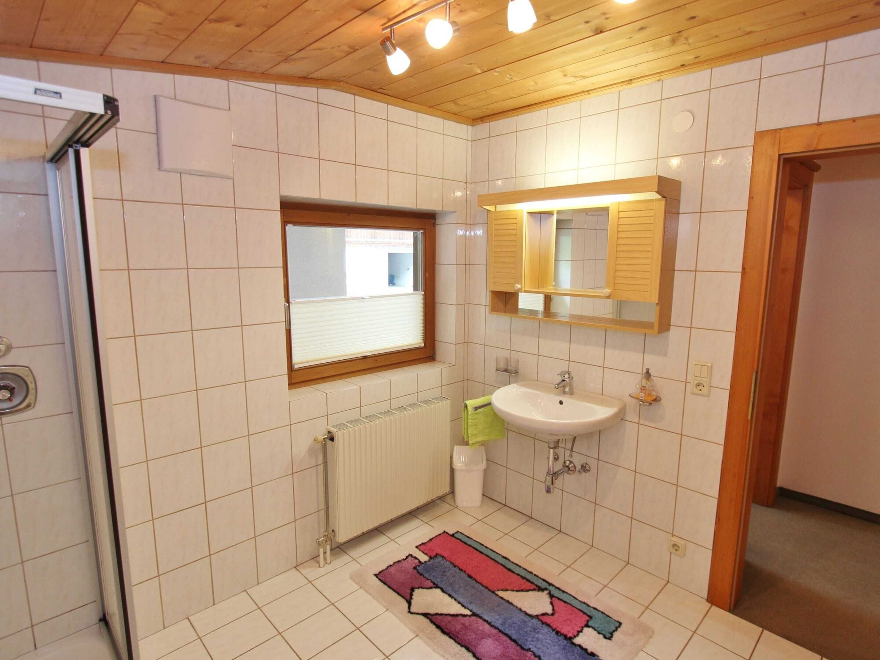 Un baño con ventana, lavamanos, espejo y radiador.