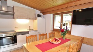 A compact kitchen with wooden cabinets, a microwave, a stove, and a dining area with a table set for four. - Apartment in Viehhofen Near Ski Lifts (Viehhofen)