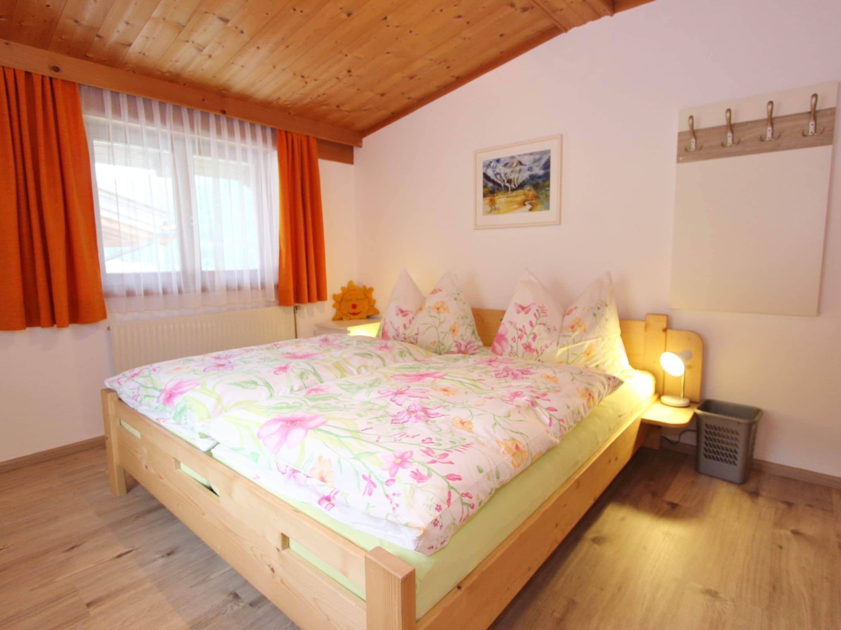 Um quarto com cama de madeira, roupa de cama floral, mesa de cabeceira com abajur e um quadro na parede.