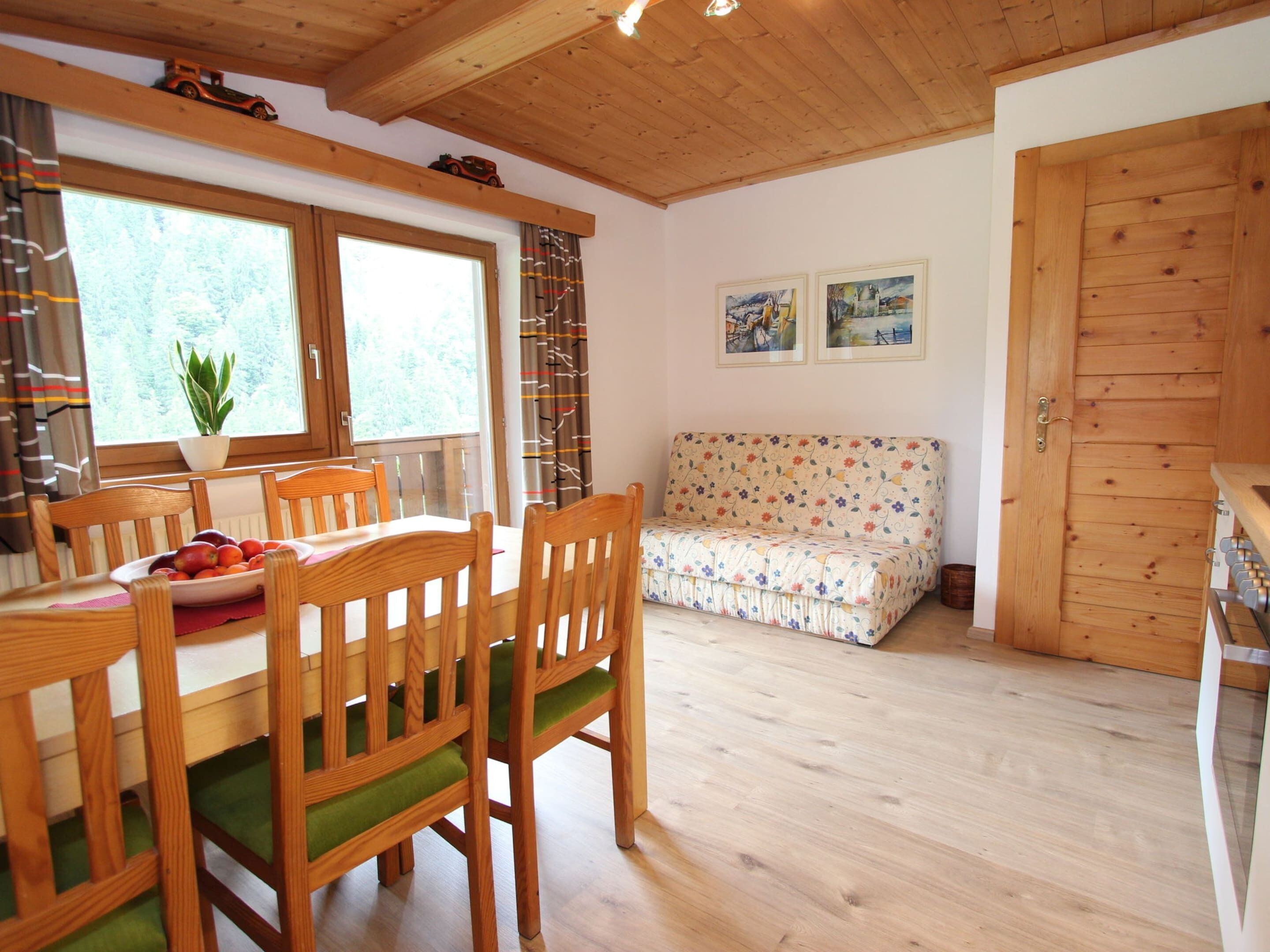 A cozy room with a wooden dining table, chairs, a sofa, and a wooden door.