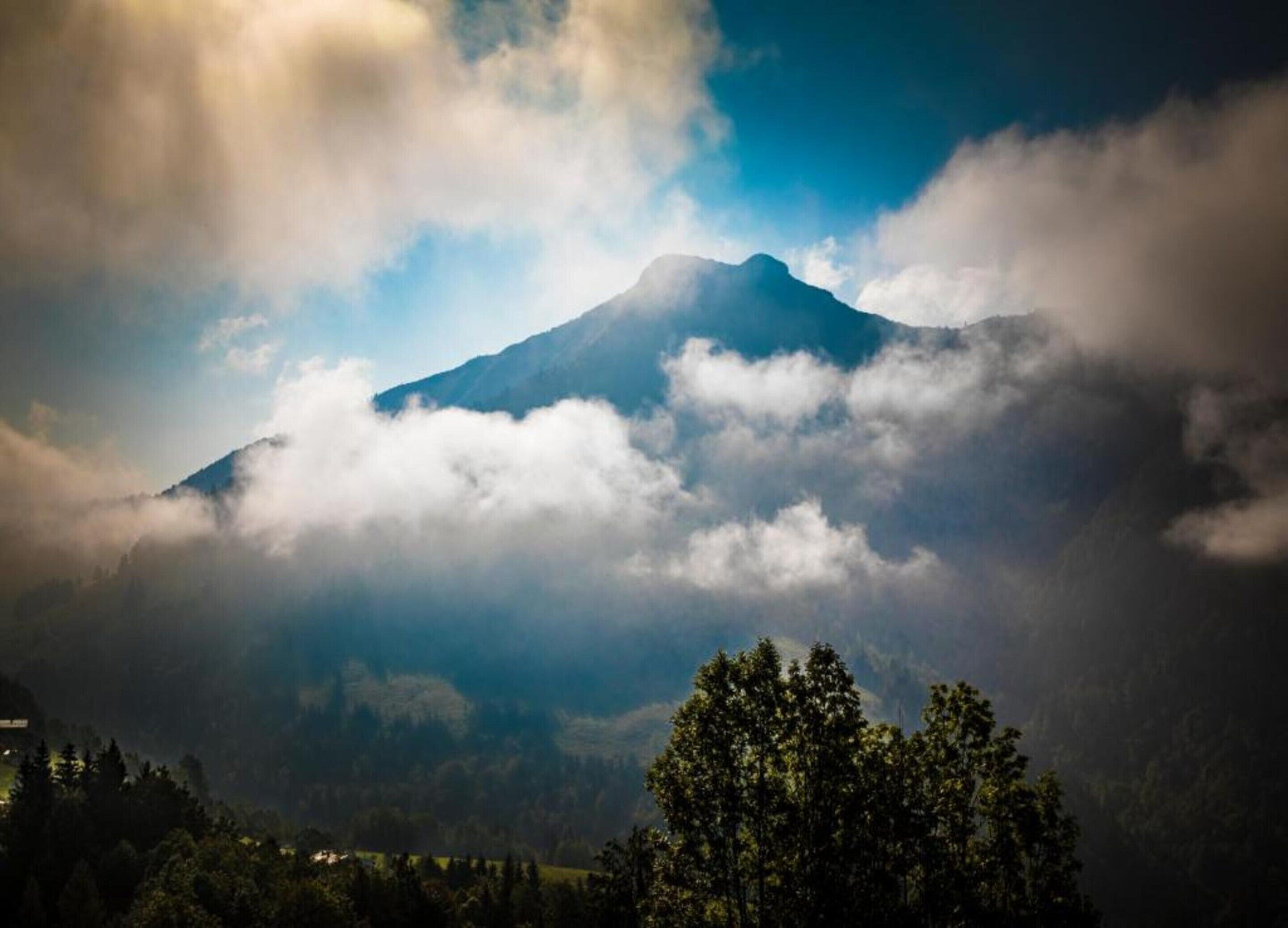 A mountain with clouds at its peak, surrounded by trees.