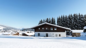 A two-story wooden house with a snow-covered roof, surrounded by a snowy landscape and evergreen trees. - Large Holiday Home With Plenty of Privacy (Flachau)