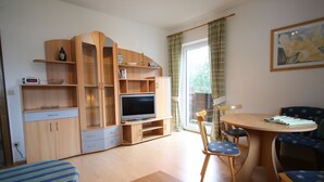 A compact living space with a TV, wooden furniture, a dining table, and a window with curtains. - Apartment in Krispl Near Ski Slopes (Krispl)