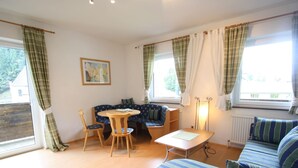 A cozy living room with a sofa, a dining table, and a chair. There is a window with curtains and a radiator. - Apartment in Krispl Near Ski Slopes (Krispl)