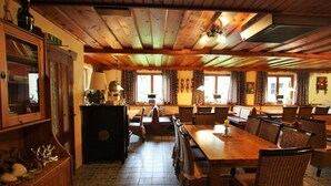 A spacious dining area with wooden tables and chairs, a central island with a lamp, and a view of the outdoors through large windows. - Apartment in Krispl Near Ski Slopes (Krispl)