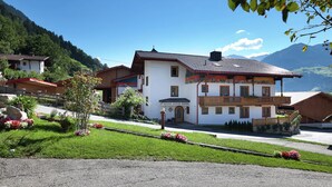Un bâtiment de style chalet traditionnel, doté d’un balcon, entouré d’un jardin bien entretenu et offrant une vue sur les montagnes.
