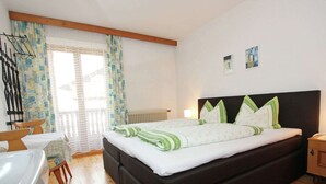 Une chambre à coucher avec un grand lit, un plancher en bois, une fenêtre avec des rideaux, un radiateur et une petite table de chevet.
