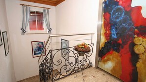 A staircase with a metal railing, a window with curtains, a framed picture, and a colorful abstract painting on the wall.