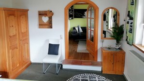 Una habitación con un armario de madera, una silla blanca, un espejo y una mesita con una planta.