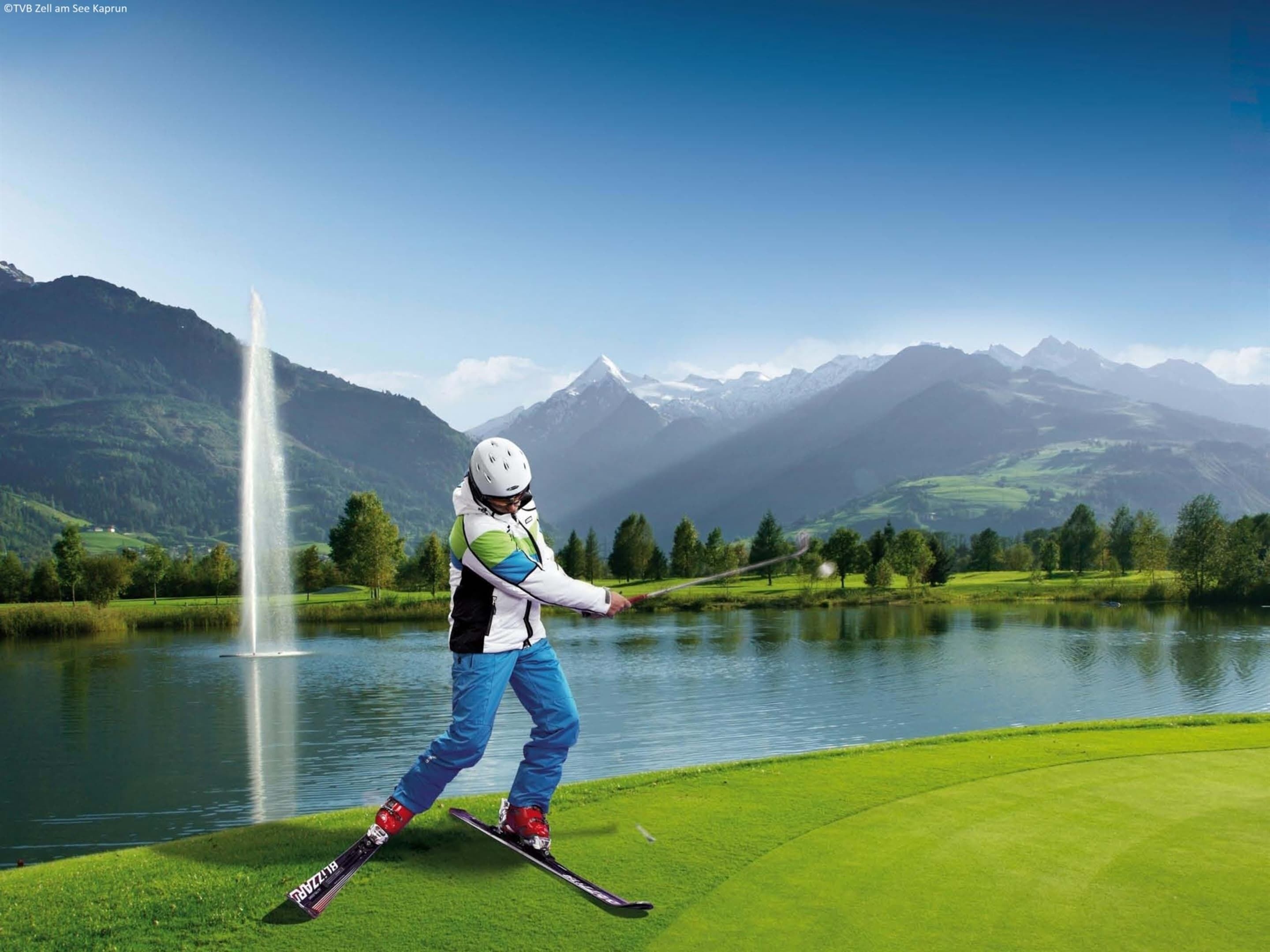 A skier on a well-maintained grassy area with a lake and mountains in the background.