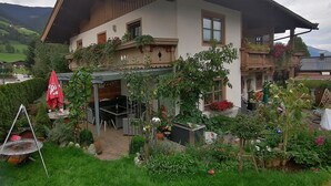 A traditional chalet with a sloped roof, a patio with outdoor furniture, and a well-maintained garden with various plants and flowers. - Apartment Walchen Near Ski Slopes (Piesendorf)