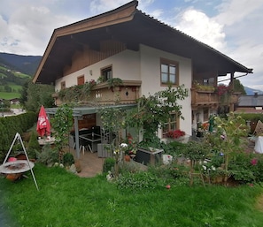 A traditional chalet with a sloped roof, a patio with outdoor furniture, and a well-maintained garden with various plants and flowers. - Apartment Walchen Near Ski Slopes (Piesendorf)