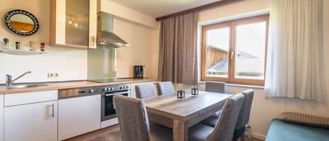 A modern kitchen with white cabinets, a stainless steel stove, and a dining table with four chairs.