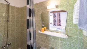 A bathroom with green tiles, a shower, a mirror with a towel, and a shelf with toiletries. - Spacious Apartment near Ski Trail in Maishofen (Maishofen)