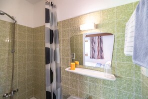 A bathroom with green tiles, a shower, a mirror with a towel, and a shelf with toiletries. - Spacious Apartment near Ski Trail in Maishofen (Maishofen)