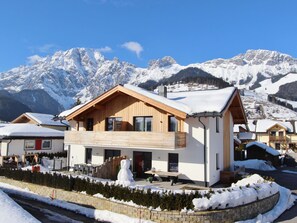 A modern chalet with a wooden facade, large windows, and a balcony, set against a backdrop of snow-covered mountains. - Holiday Home in ski Area in Leogang With Sauna (Leogang)
