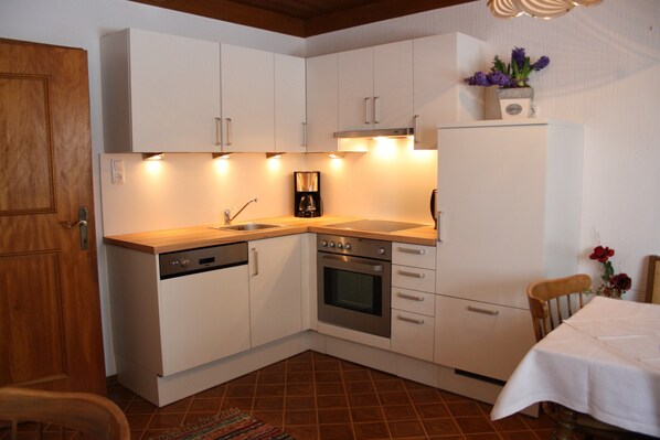 Kitchen features a dishwasher, oven, coffee maker, and sink, with a table and chair for dining.