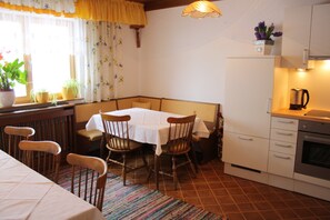 A kitchen with a dining table, chairs, a coffee maker, and a refrigerator.