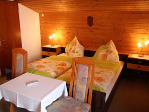 Two single beds with floral bedding, each flanked by a nightstand with a lamp, and a small table in front.