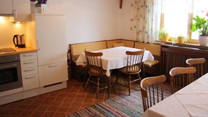 Une cuisine compacte avec un coin repas, comprenant une table pour quatre personnes, des chaises, une machine à café et une fenêtre avec des rideaux.