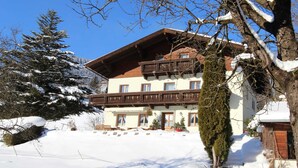 Un immeuble à plusieurs étages doté d’un balcon en bois, entouré d’arbres couverts de neige et surplombant un ciel bleu clair.