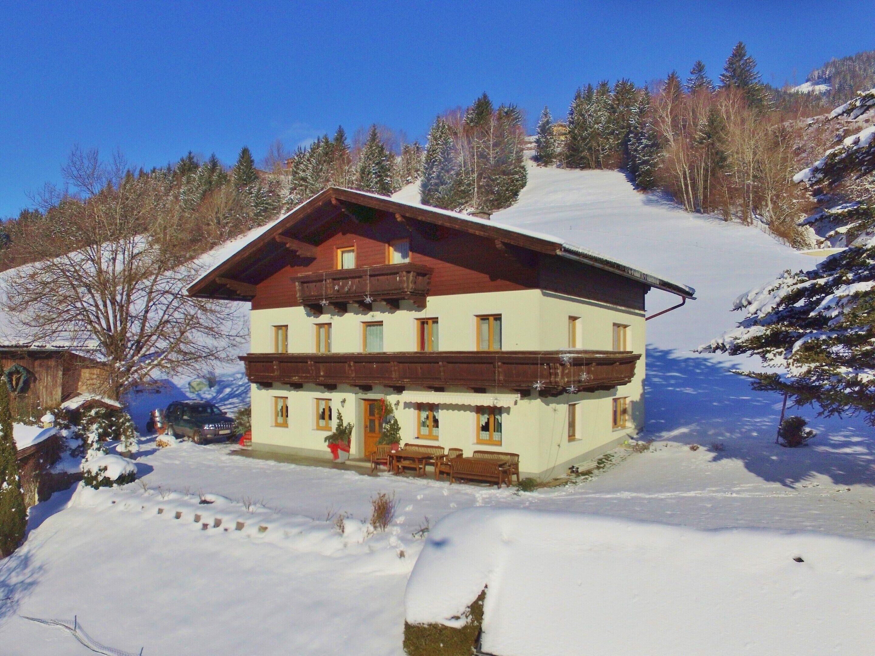 A two-story chalet with a balcony, surrounded by snow-covered trees and a ski slope.