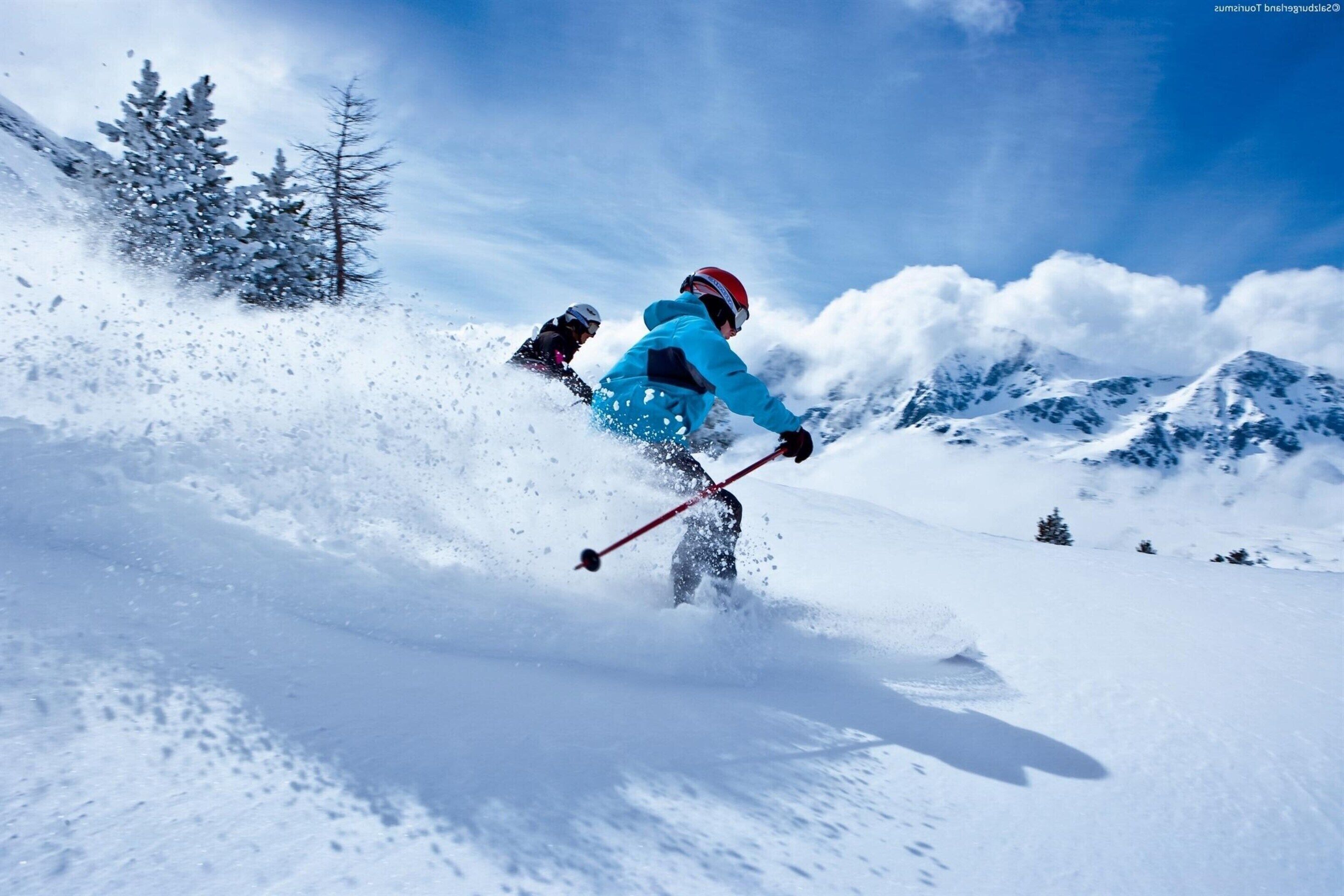 A person skiing down a snowy slope with trees and mountains in the background.