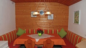 Een gezellig eetgedeelte met een houten tafel, twee stoelen en een bank met gestreepte kussens.