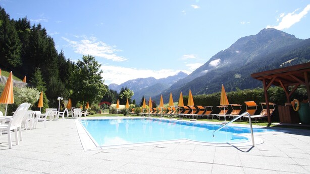 A pool area with lounge chairs and umbrellas, surrounded by mountains. - Simplistic Apartment in Kleinar near Cross Country Skiing (Kleinarl)