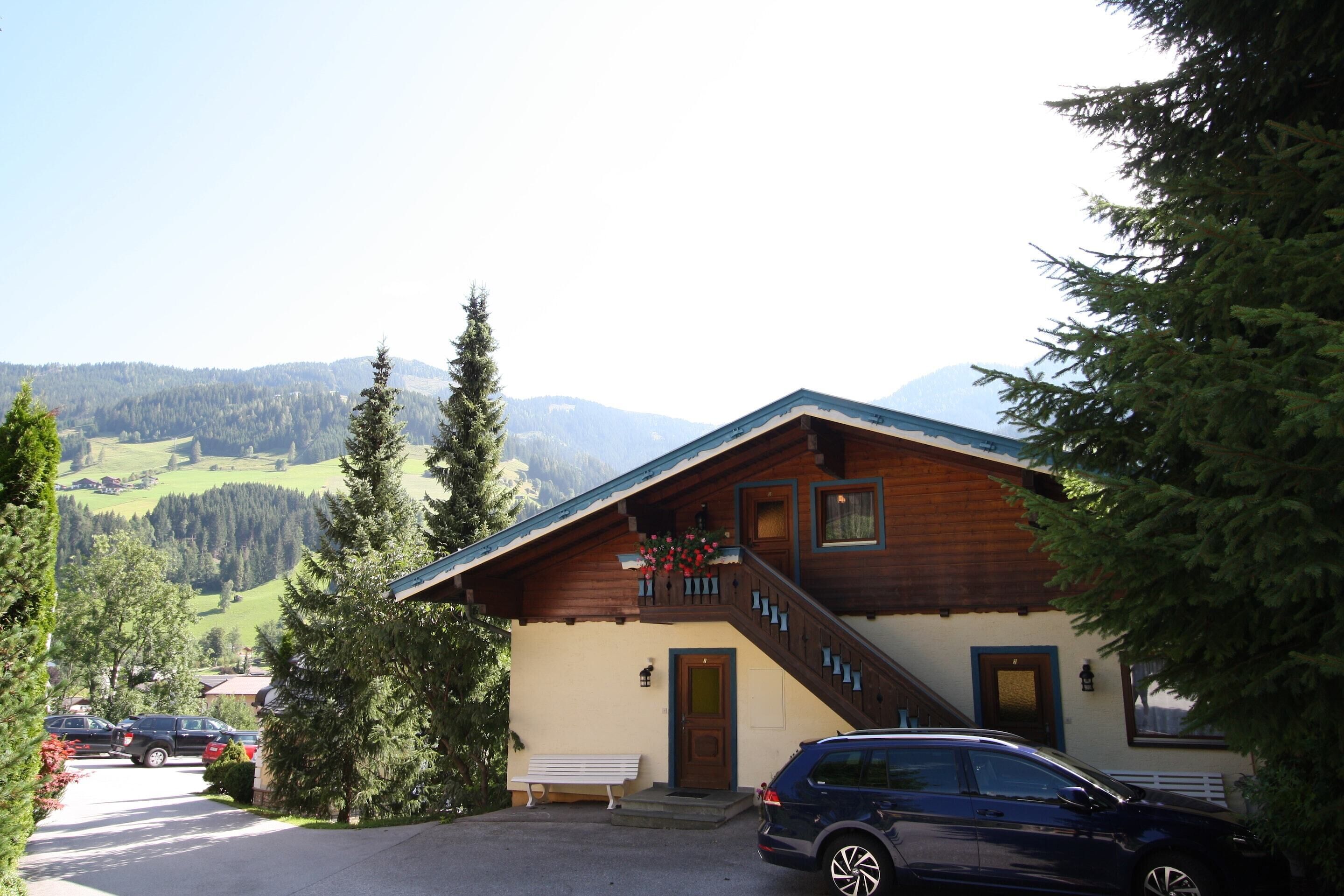 A mountain lodge with a wooden exterior, a staircase leading to the entrance, and a view of the surrounding mountains.
