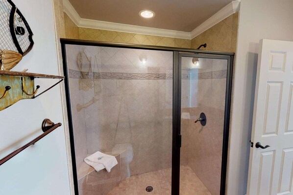 Ducha con cerramiento de vidrio, una toalla blanca en el suelo, una puerta con manija y un toallero de pared.