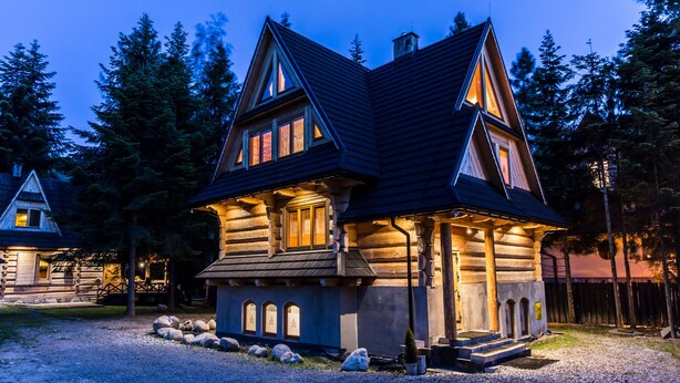 A log cabin with a steeply pitched roof, multiple windows, and a porch area. - Zakopiana (Zakopane)