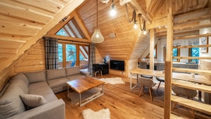 A cozy loft-style room with a wooden ceiling, a gray sofa, a wooden dining table, and a TV. - Zakopiana (Zakopane)